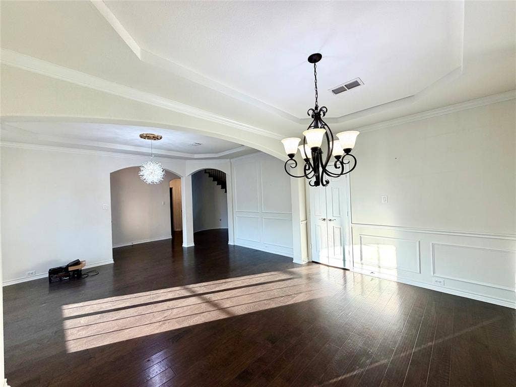 4514 Sea Sparrow Lane, Garland, TX 75043 Tray ceilings with crown molding, dark wood-finish flooring, decorative wall paneling, and intricate metal chandeliers