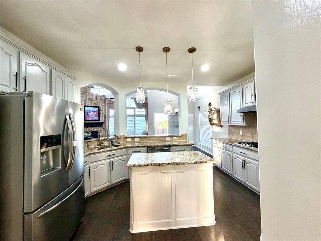 4514 Sea Sparrow Lane, Garland, TX 75043 Kitchen featuring a central island with a stone-finish countertop, white cabinetry with matching hardware, stainless steel refrigerator, recessed lighting, and three glass pendant fixtures