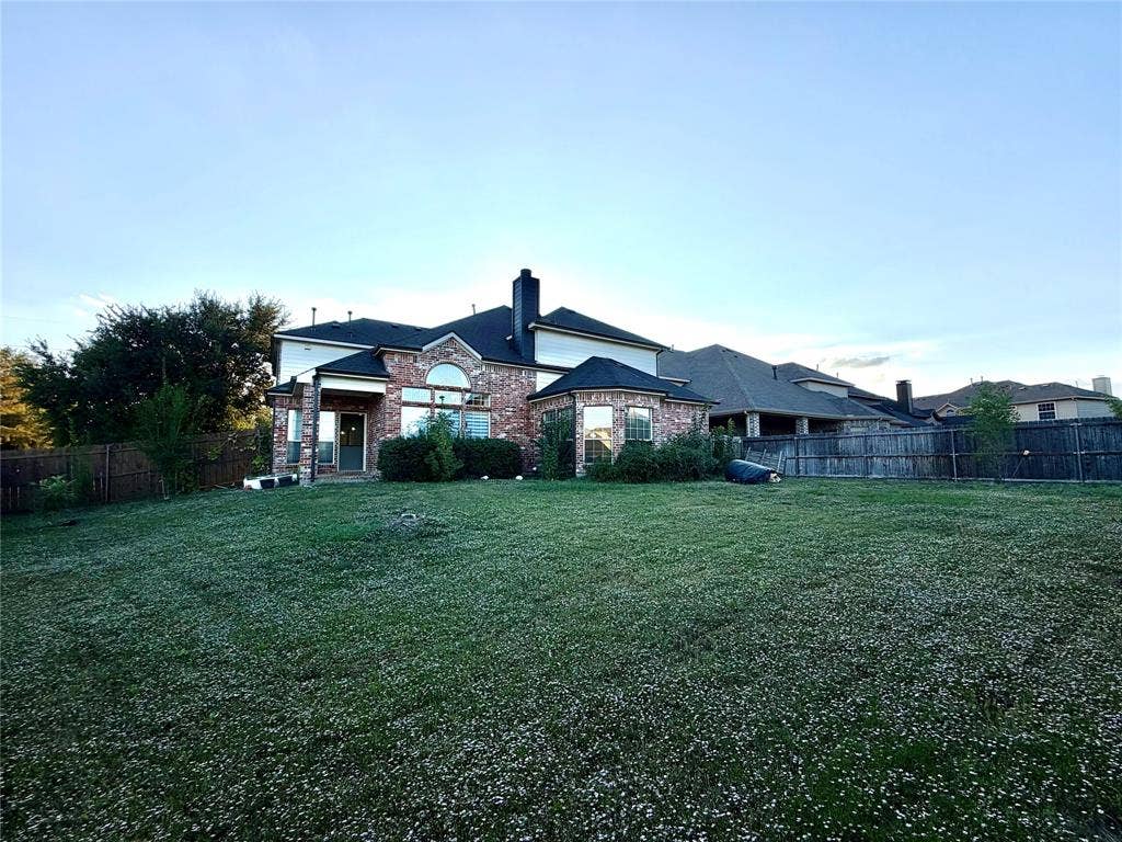 4514 Sea Sparrow Lane, Garland, TX 75043 Brick exterior featuring multi-gabled rooflines, arched window detailing, and a spacious rear yard enclosed by wood privacy fencing