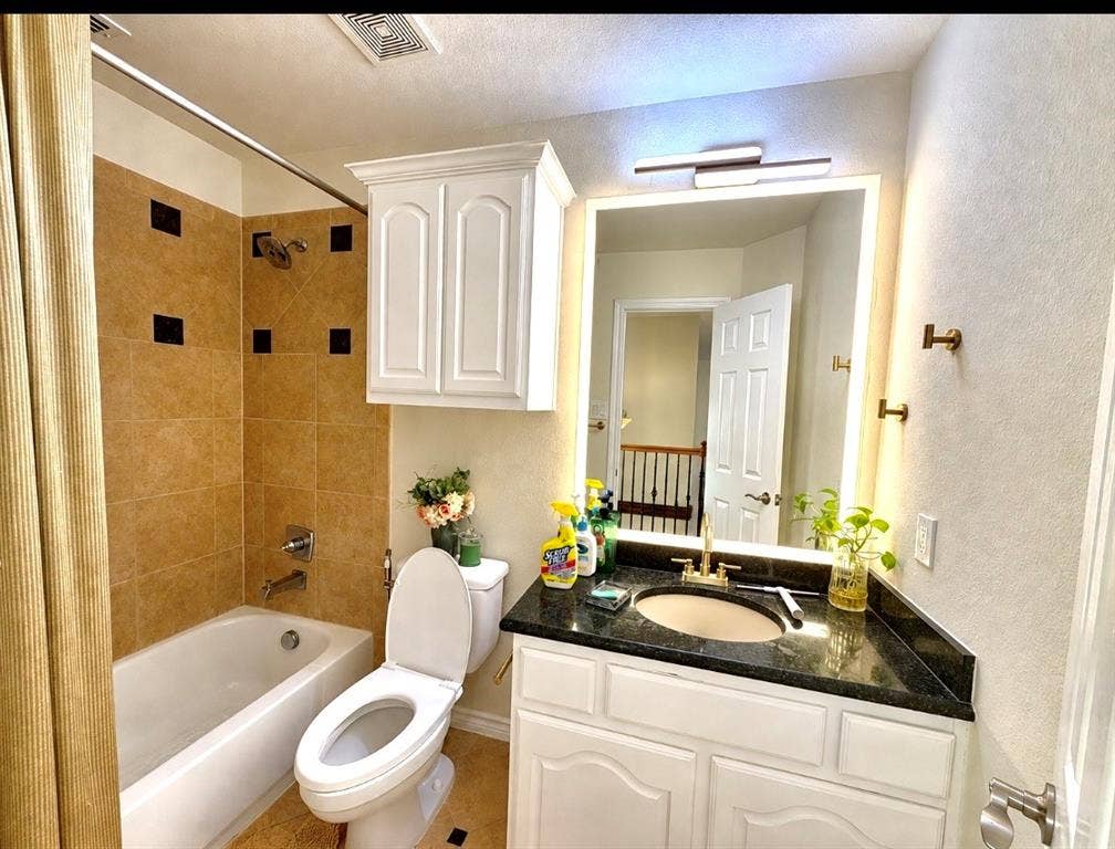 4514 Sea Sparrow Lane, Garland, TX 75043 Bathroom featuring a vanity with dark stone countertop, undermount sink, and brass-tone hardware, paired with a wall-mounted medicine cabinet, backlit mirror, and a tile-surround tub