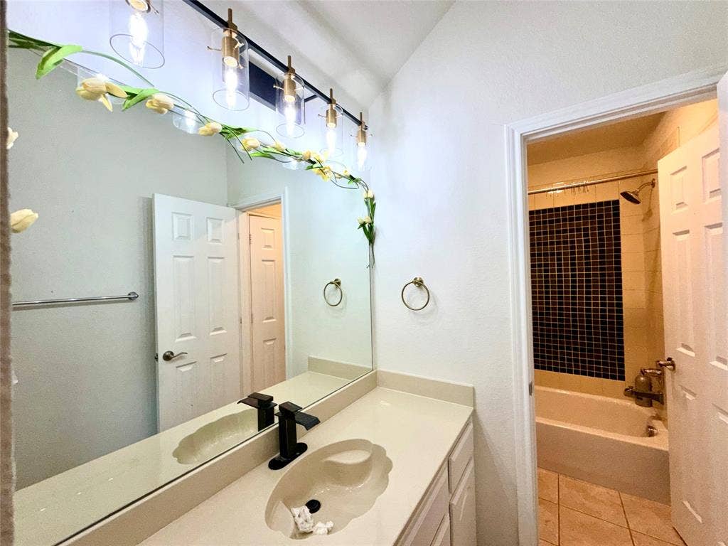4514 Sea Sparrow Lane, Garland, TX 75043 Bathroom featuring an integrated vanity countertop with an oval basin, matte black faucet, four-light glass vanity fixture, and a tiled shower surround