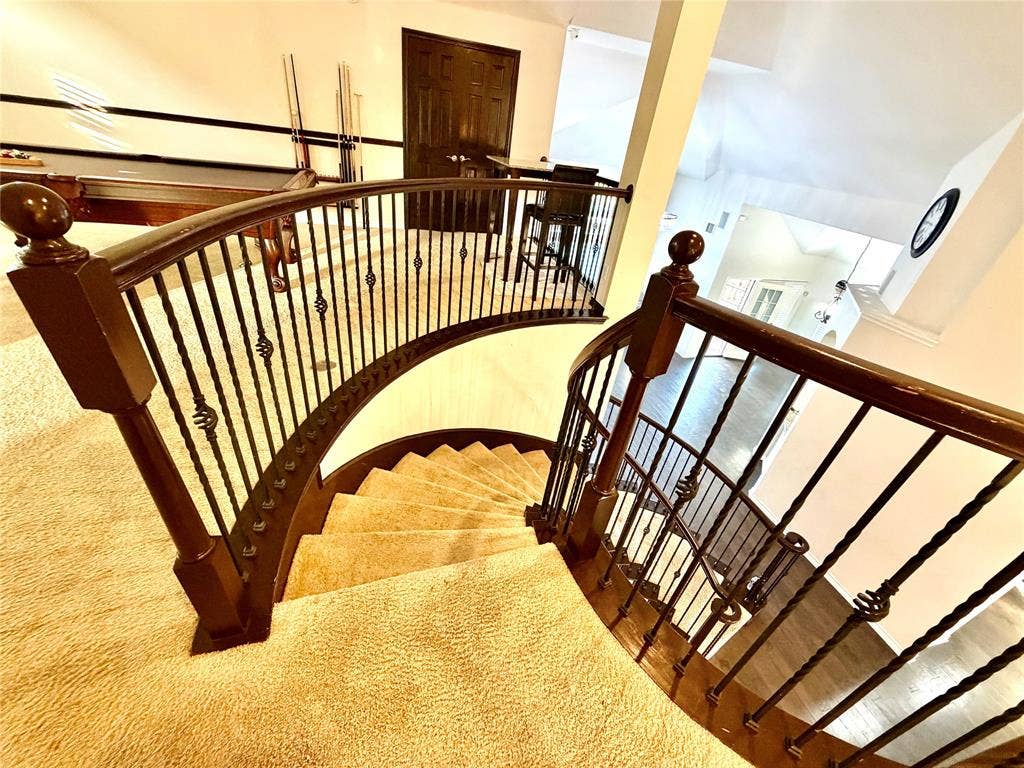 4514 Sea Sparrow Lane, Garland, TX 75043 Curved staircase featuring custom wrought iron balusters, a dark wood-finish handrail, carpeted treads, and architectural vaulted ceilings