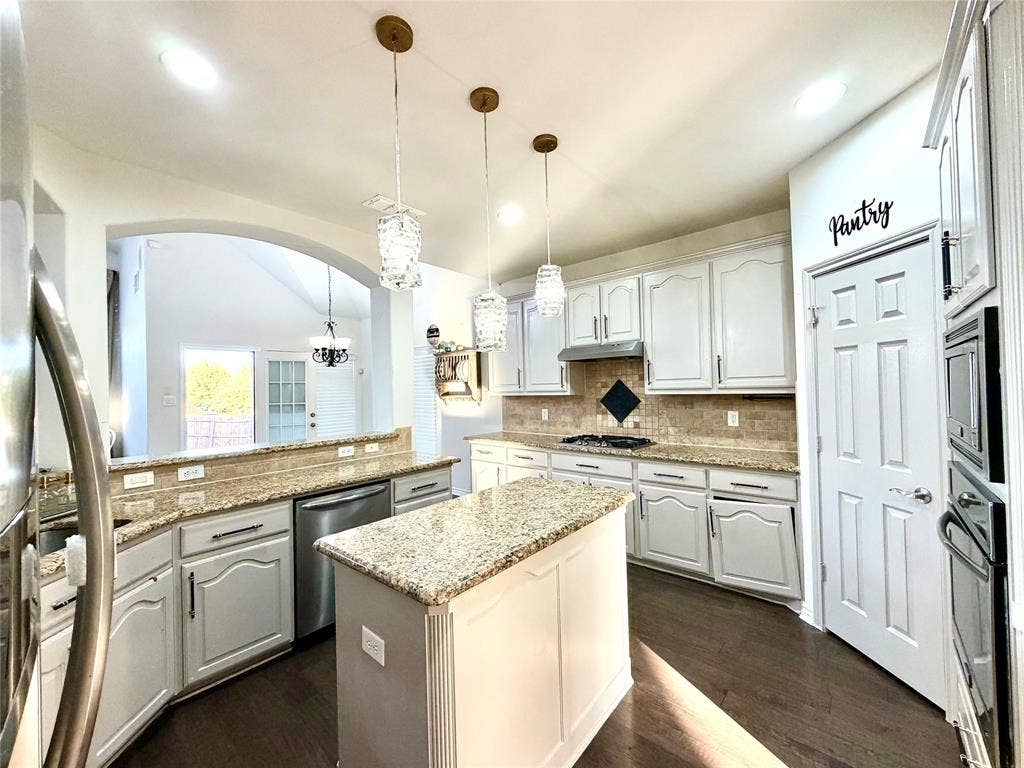 4514 Sea Sparrow Lane, Garland, TX 75043 Kitchen featuring light-toned cabinetry, stone-finish countertops, tile backsplash, wood-finish flooring, and a center island with three glass pendant lights