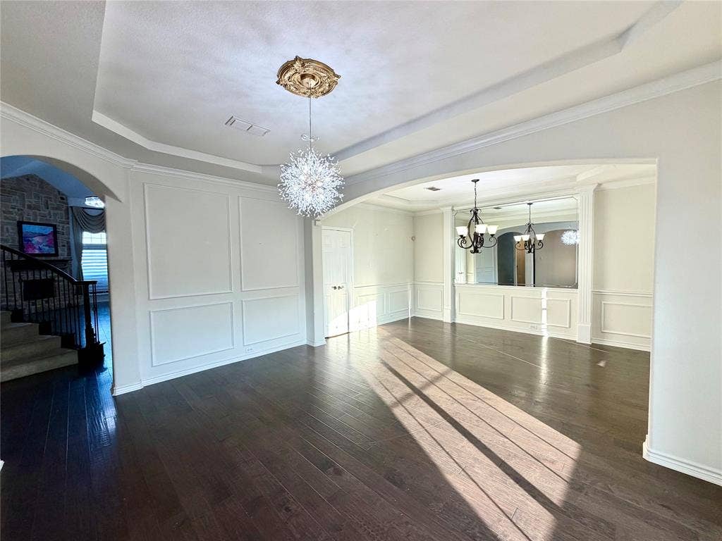 4514 Sea Sparrow Lane, Garland, TX 75043 Tray ceiling with central medallion, wood-finish flooring, wainscoting paneling, multi-tiered crystal-style chandelier, and recessed lighting