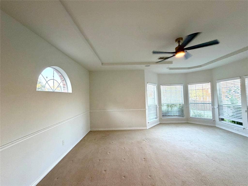 4514 Sea Sparrow Lane, Garland, TX 75043 Tray ceiling with a central multi-blade light fixture, arched accent window, chair rail molding, and multiple windows with horizontal blinds