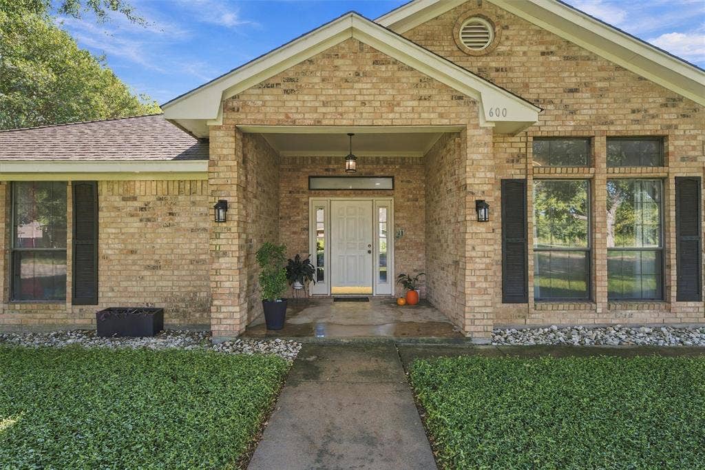 Single-story brick exterior featuring a covered front entryway, multi-pane entry door with sidelights, dark decorative shutters, and a concrete walkway