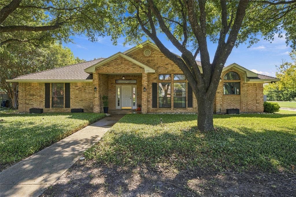 Single-story brick exterior featuring a covered entryway, arched window, and mature shade trees