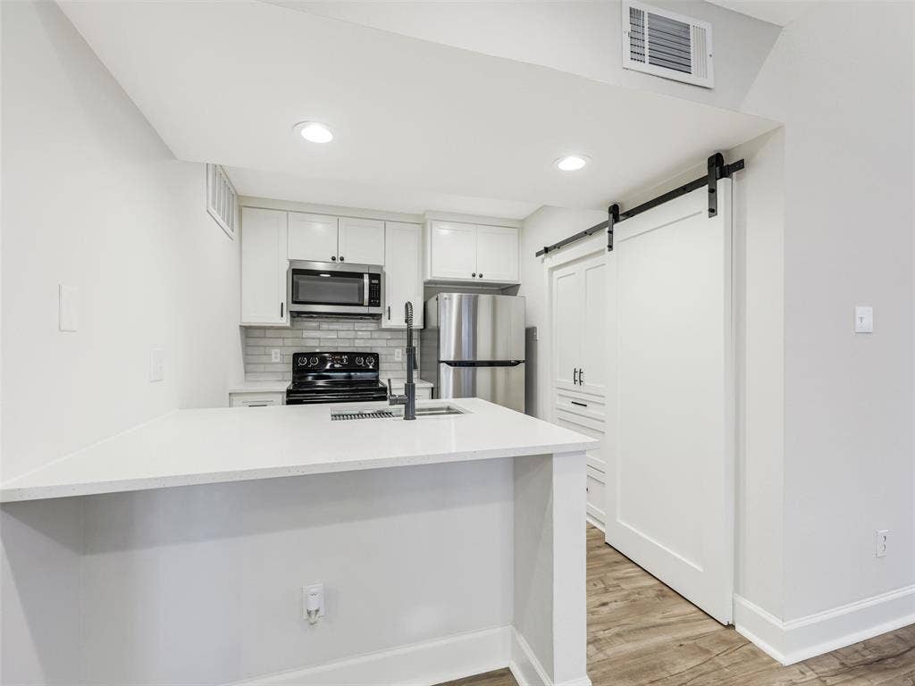 449 Harris Street, #102L, Coppell, TX 75019 Kitchen featuring a stone-surface breakfast bar, white cabinetry, stainless steel appliances, subway tile backsplash, and a sliding barn door