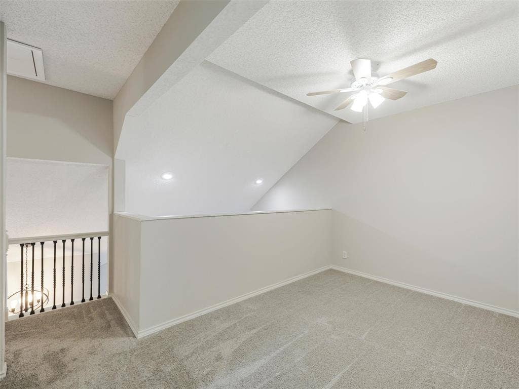 449 Harris Street, #102L, Coppell, TX 75019 Vaulted ceiling, neutral wall tones, textured ceiling finish, ceiling fan with light fixture, and black metal spindle railing