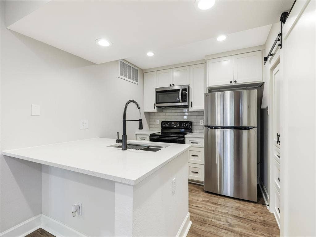 449 Harris Street, #102L, Coppell, TX 75019 Kitchen featuring white shaker-style cabinetry, solid-surface countertops, stainless steel appliances, matte black plumbing fixtures, and wood-finish flooring