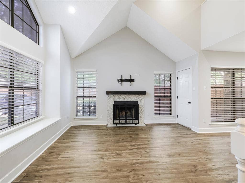 449 Harris Street, #102L, Coppell, TX 75019 Vaulted ceilings featuring a fireplace with a chevron-pattern tile surround and a dark wood mantel, wood-finish flooring, and expansive windows with built-in window seating