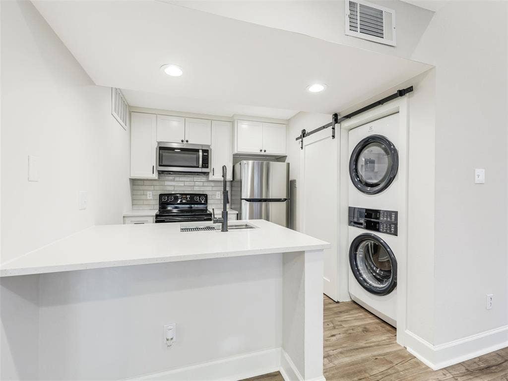 449 Harris Street, #102L, Coppell, TX 75019 Kitchen featuring white cabinetry, solid-surface countertops, subway tile backsplash, stainless steel appliances, and wood-finish flooring with a barn-style sliding door concealing a laundry area