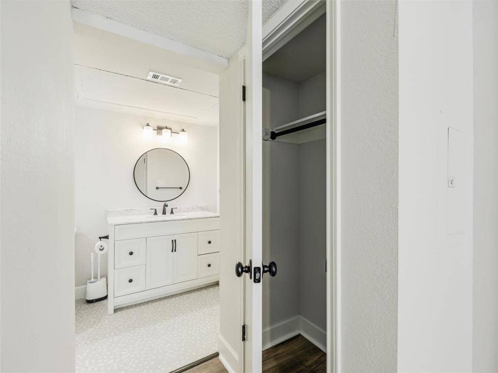449 Harris Street, #102L, Coppell, TX 75019 Bathroom featuring a white vanity with drawers, a round mirror, three-light fixture, and patterned flooring, complemented by a storage closet with a built-in rod and shelf