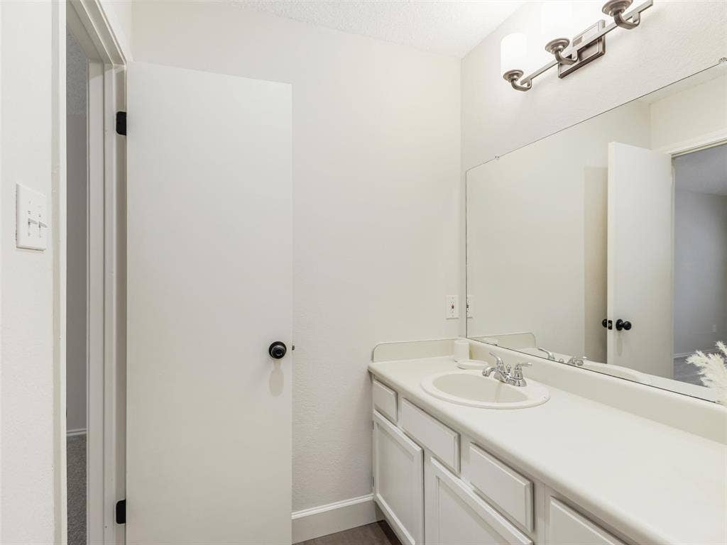 449 Harris Street, #102L, Coppell, TX 75019 Vanity with a solid-surface countertop and integrated basin, large wall-mounted mirror, and multi-bulb vanity light fixture