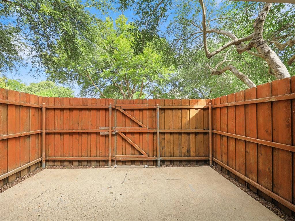 449 Harris Street, #102L, Coppell, TX 75019 Concrete patio enclosed by a wood privacy fence featuring a functional access gate and mature tree canopy