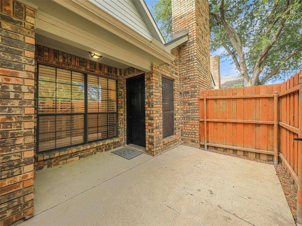 449 Harris Street, #102L, Coppell, TX 75019 Brick exterior patio featuring a concrete slab, floor-to-ceiling brick chimney, dark-trimmed windows, and a wood privacy fence