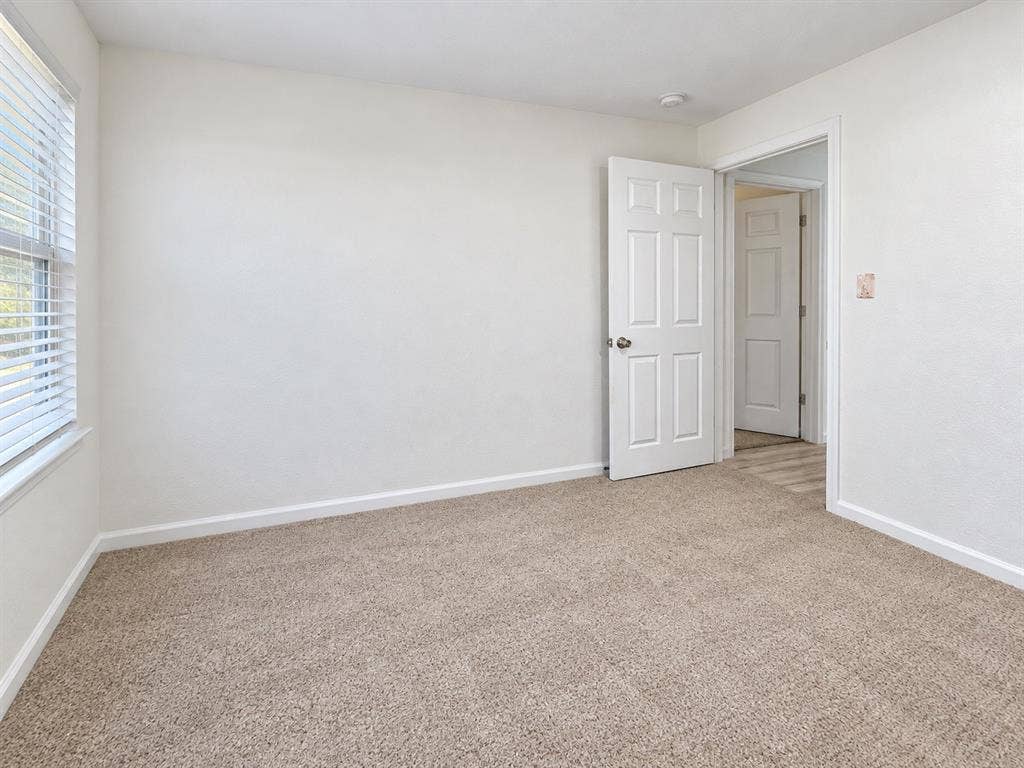 Neutral-toned carpet, white walls, and six-panel interior doors, with white horizontal blinds over the window