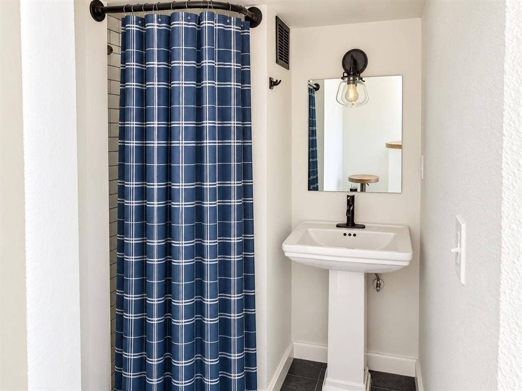 White pedestal sink with a matte black faucet, wall-mounted light fixture, and dark tile flooring