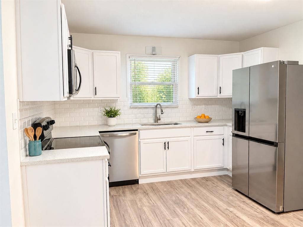 Kitchen featuring white shaker-style cabinetry, stainless steel appliances, light-toned stone countertops, subway tile backsplash, and wood-finish flooring