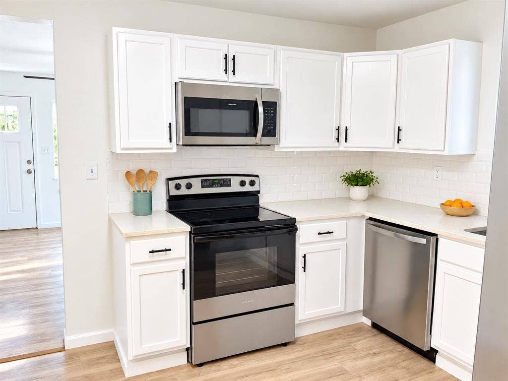 Kitchen featuring white shaker-style cabinetry, stainless steel appliances, subway tile backsplash, light-toned stone-finish countertops, and wood-finish flooring
