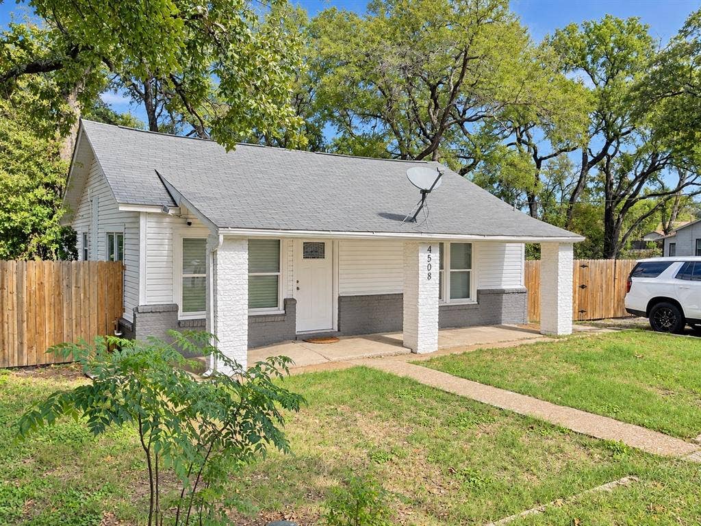 Single-story exterior featuring horizontal siding, a covered front porch with stone-finish pillars, and wood privacy fencing