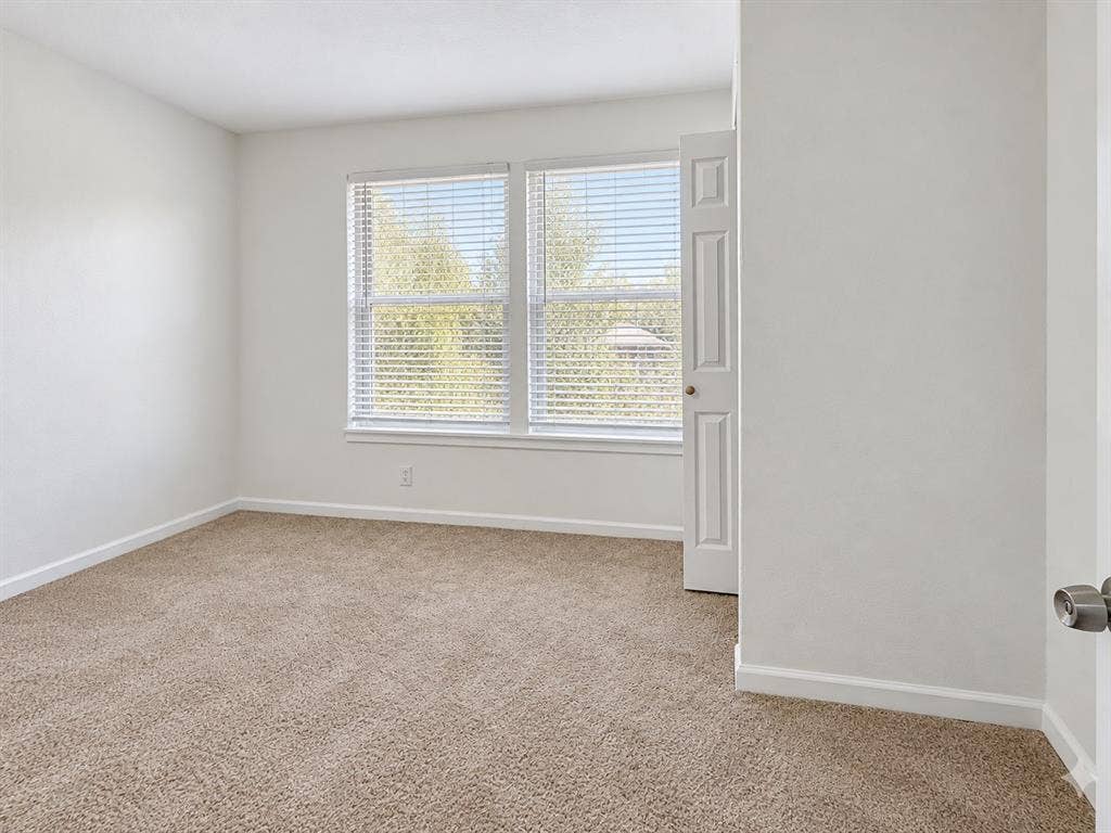 Neutral-toned wall paint, wall-to-wall carpeting, and double-pane windows equipped with horizontal blinds