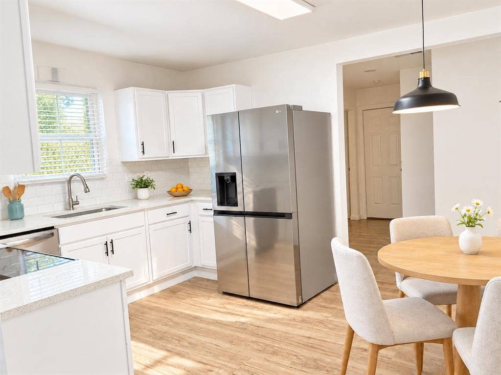 Kitchen featuring white shaker-style cabinetry, white subway tile backsplash, stainless steel refrigerator, and wood-finish flooring with a pendant light fixture above the dining area