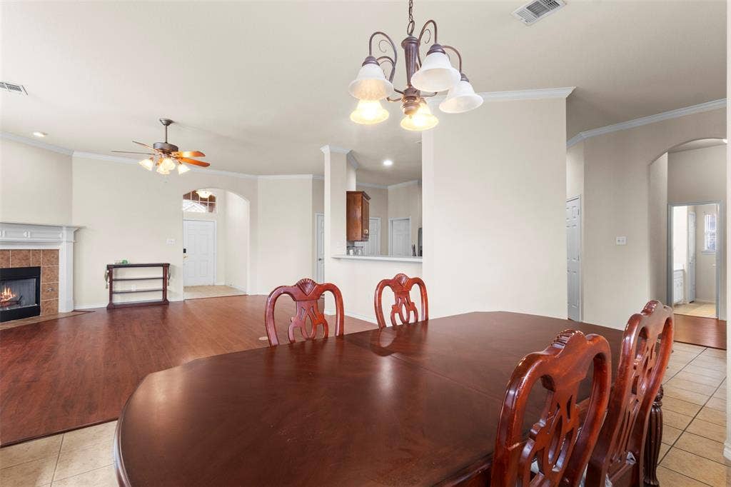 Open floor plan featuring wood-finish flooring, a fireplace with a mantel and tiled surround, crown molding, and a suspended chandelier