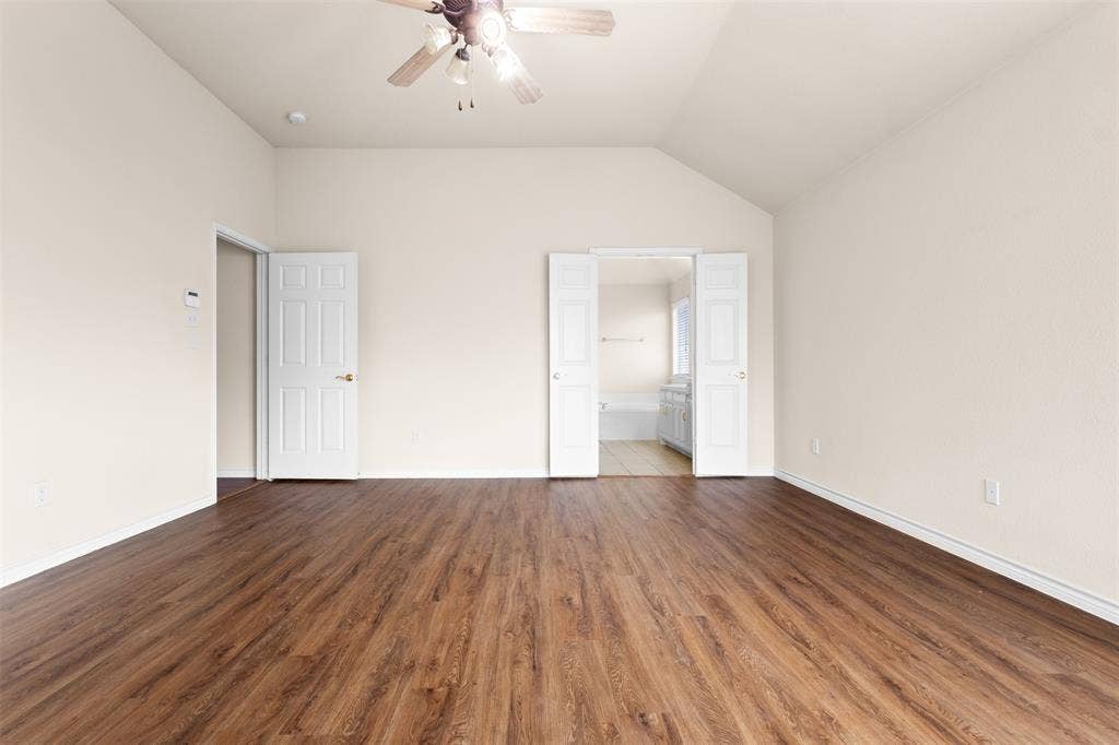 Room featuring vaulted ceilings, wood-finish flooring, a ceiling fan, and white paneled doors