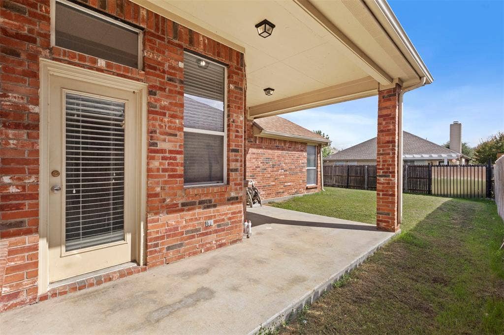 Covered concrete patio featuring red brick exterior siding, recessed ceiling lighting, and a single-light glass panel door with a transom window