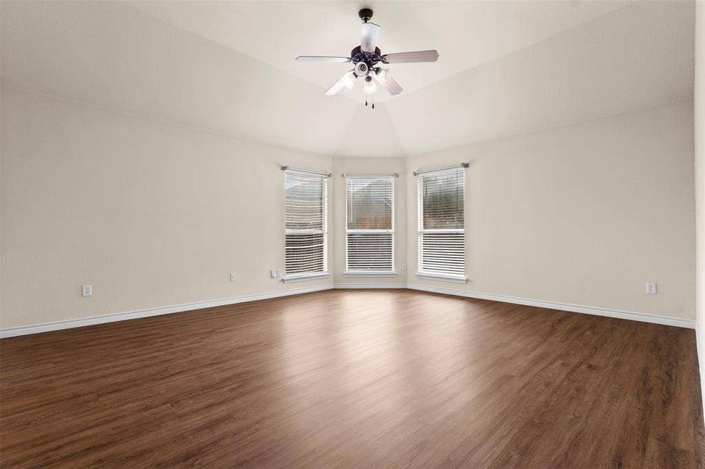 Vaulted ceiling featuring a central multi-blade ceiling fan, wood-finish flooring, and a bay of three windows