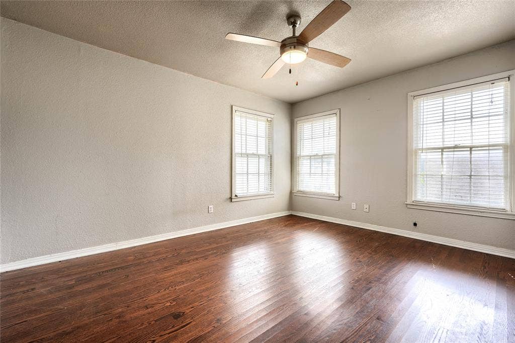 Interior space featuring wood-finish flooring, three double-hung windows, and a ceiling fan with integrated lighting