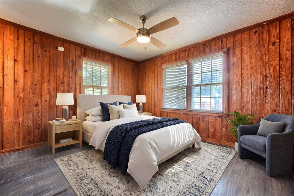 Wood-paneled walls, neutral wood-finish flooring, multi-pane windows, and a central ceiling fan with an integrated light fixture