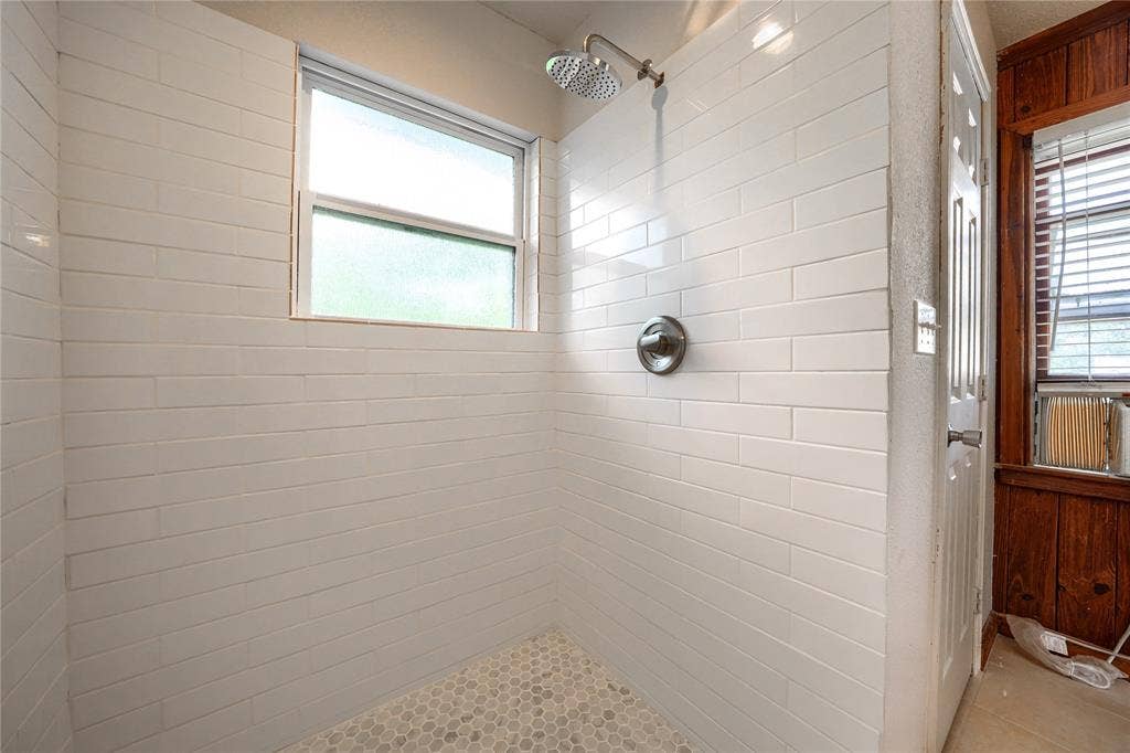 Walk-in shower enclosure featuring white subway tile wall surround, stone-finish penny tile flooring, and a circular wall-mounted shower head