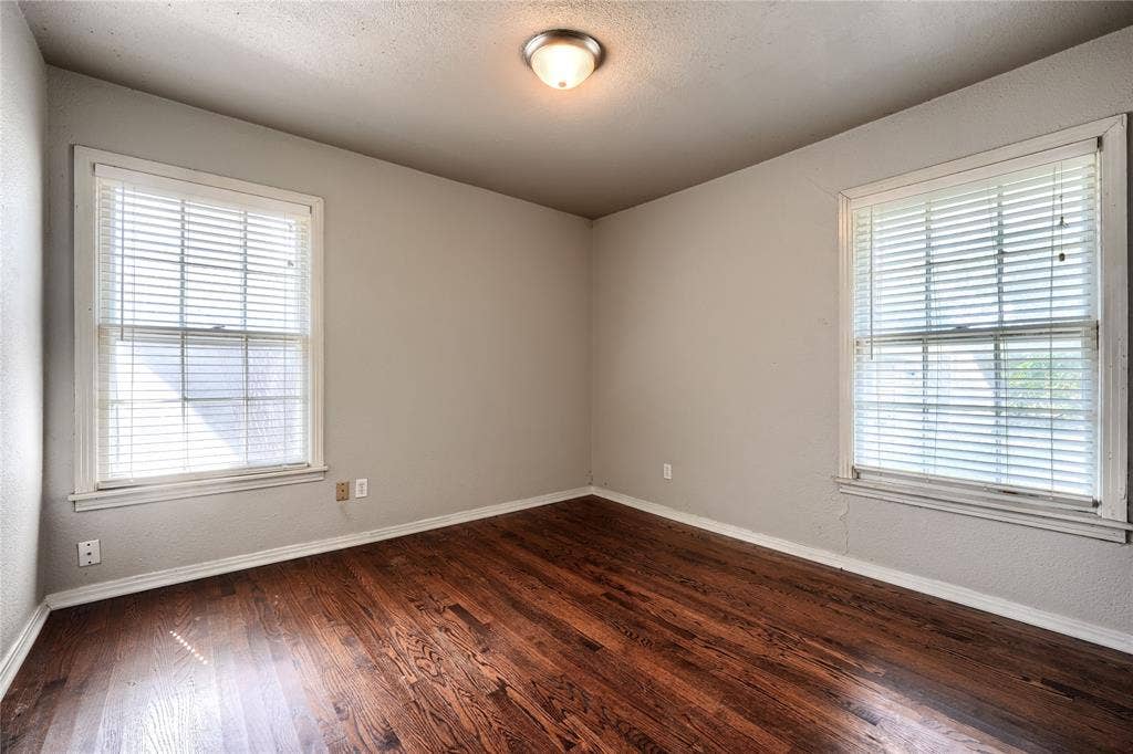 Room featuring wood-finish flooring, dual windows with fitted blinds, and a flush-mount ceiling light fixture