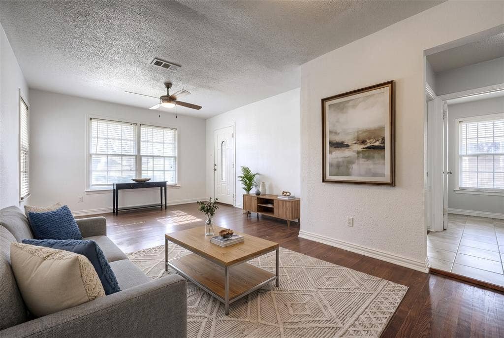 Living area featuring wood-finish flooring, ceiling fan with integrated lighting, dual-pane windows, and a panelled front entry door