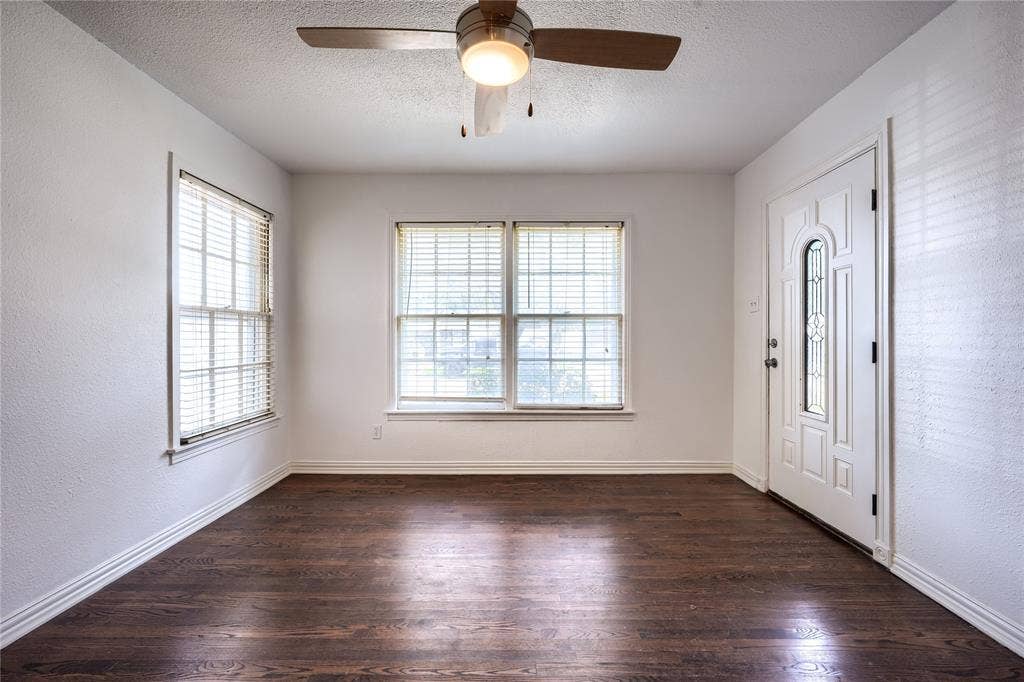 Interior space featuring dark-toned wood-finish flooring, multi-pane windows, and a white entry door with an arched glass insert, complemented by a central ceiling fan with an integrated light fixture