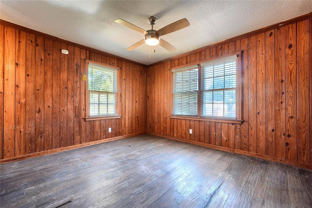Interior room featuring natural wood-paneled walls, wood-finish flooring, two sets of double-pane windows, and a central ceiling fan with an integrated light fixture