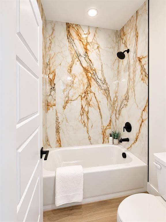 Full-height, large-format tile surround with bold veining, white soaking tub, matte black shower fixtures, and wood-finish flooring