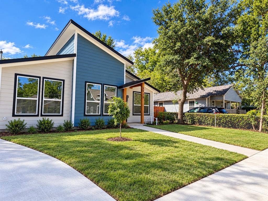 Modern architectural exterior featuring mixed-material horizontal siding, a mono-pitch roofline, expansive multi-pane windows with dark trim, and an exposed timber entryway support