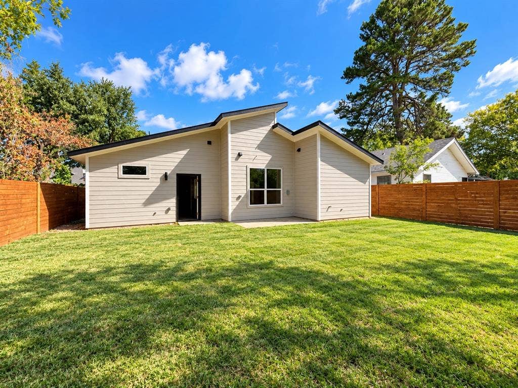 Rear exterior featuring horizontal lap siding, an asymmetrical roofline, a concrete patio, and a fenced backyard