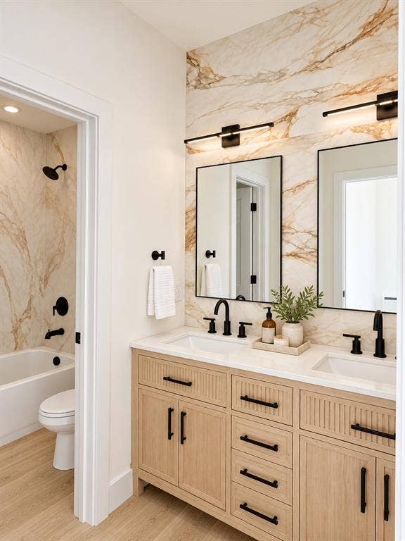 Dual-sink vanity featuring light wood-finish cabinetry, white countertops, and matte black fixtures, paired with floor-to-ceiling stone-look wall cladding and integrated linear lighting