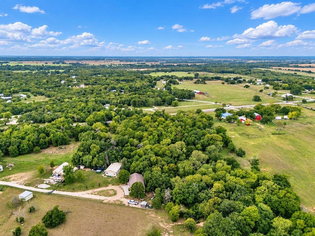 Expansive acreage featuring mature tree clusters, cleared pasture land, gravel access roads, and multiple structural improvements