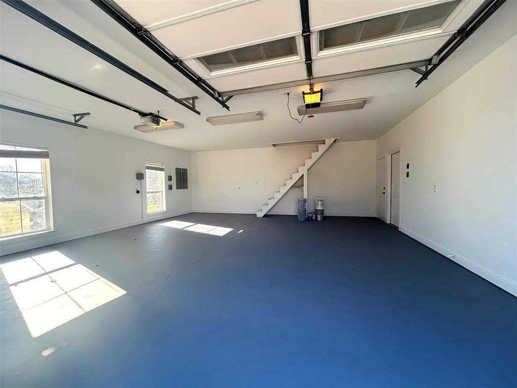 Spacious multi-car garage featuring finished epoxy flooring, dual windows, overhead lighting, and an integrated staircase