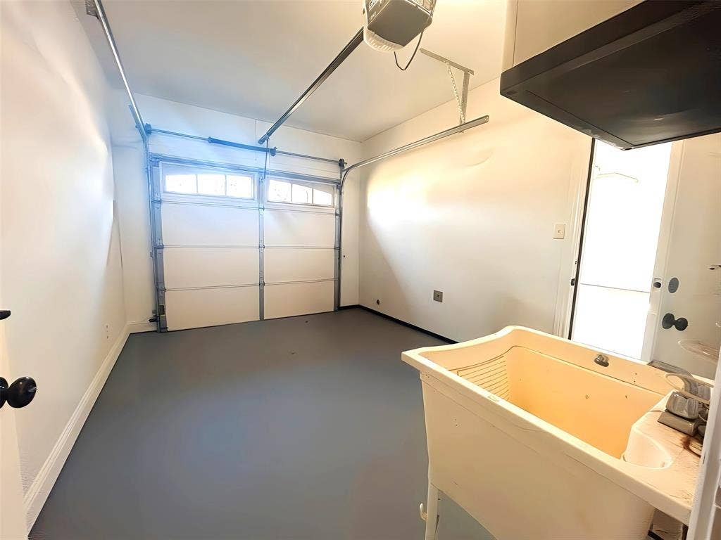 Garage featuring a sectional overhead door with transom windows, finished grey flooring, and a freestanding utility sink