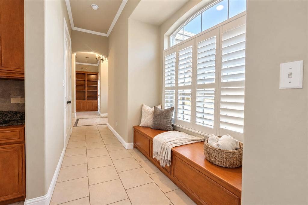 Built-in wood window bench, arched entryway, ceramic tile flooring, plantation shutters, and recessed wall shelving