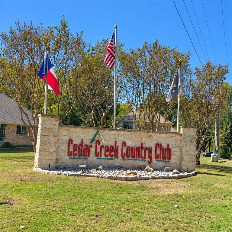 Stone monument entrance signage featuring metal lettering and three flagpoles set in a landscaped lawn