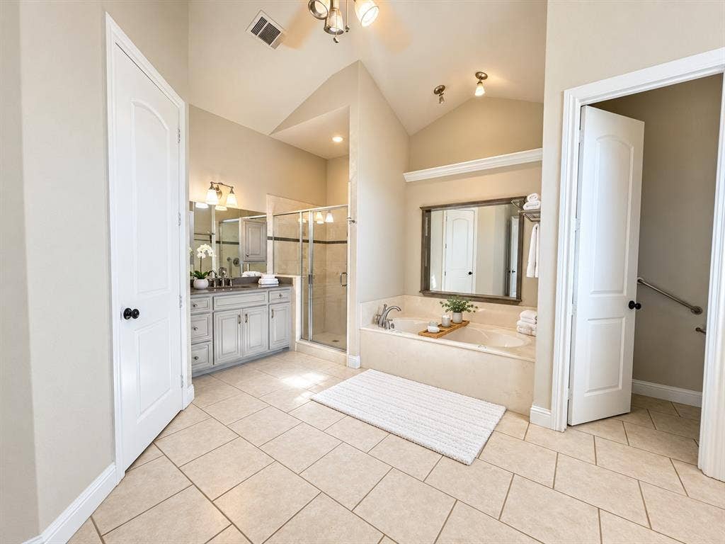 Bathroom featuring a vaulted ceiling, stone-finish tile flooring, built-in soaking tub, separate glass-enclosed shower, and cabinetry with stone countertop