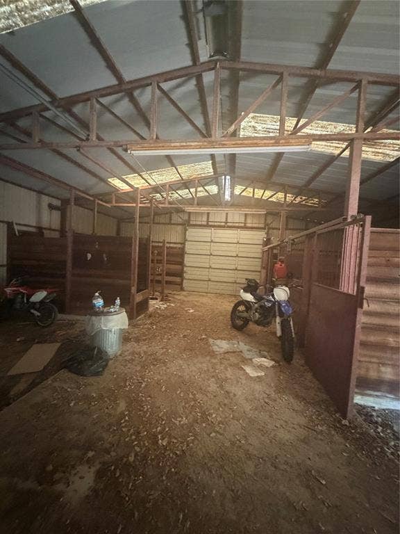 Stable featuring multiple wood-paneled stalls, exposed truss ceiling, translucent roof paneling, and a large metal roll-up door