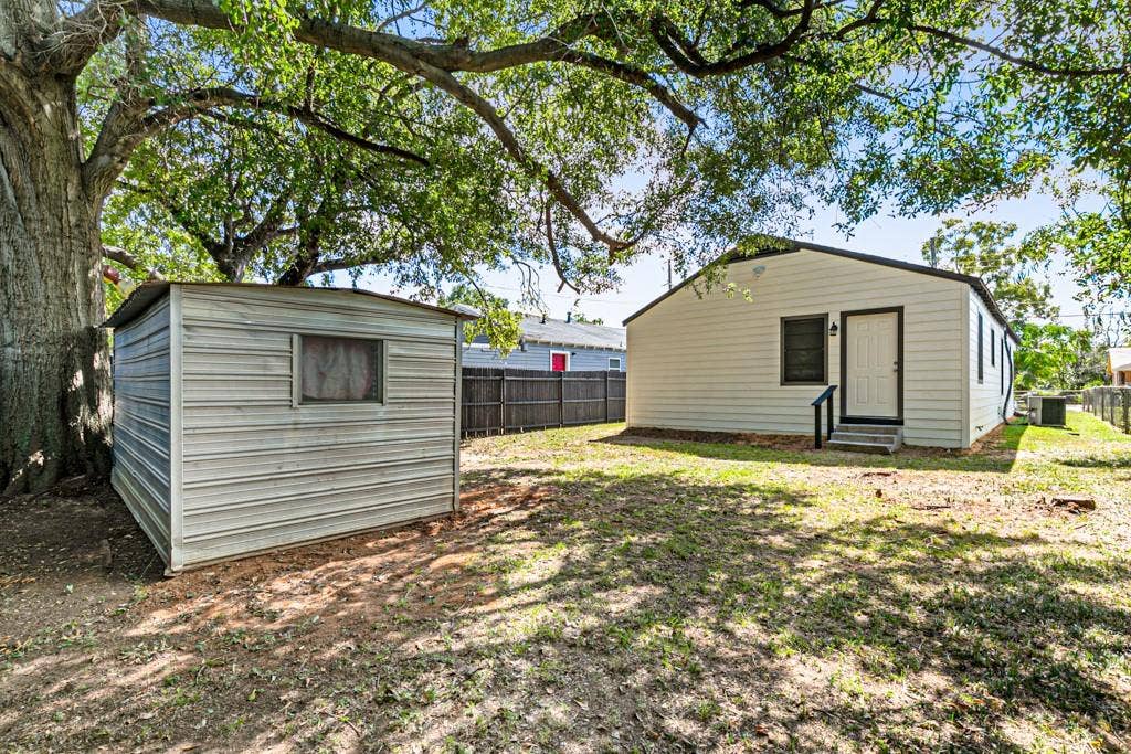 5140 Dimple Jackson Street, Dallas, TX 75210 Rear exterior view featuring a spacious backyard, mature shade trees, and a separate storage shed.